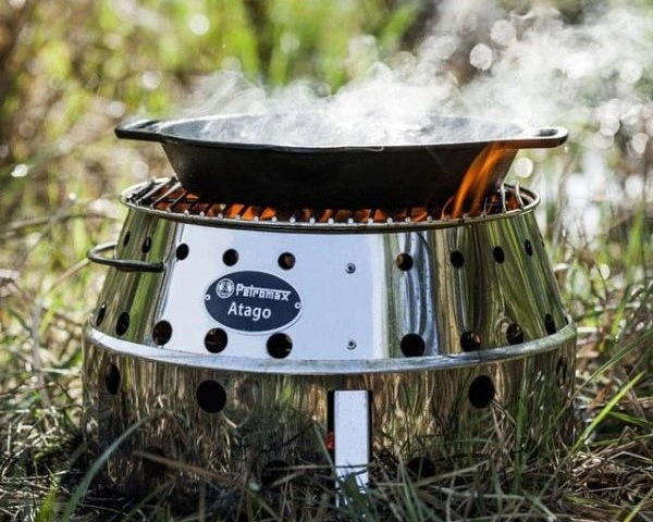Tigaie din fonta din care iasa aburi asezata pe gratar Petromax pe iarba