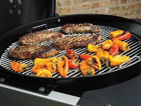 Bucati de carne si legume pe grilajul de gatit al gratarului pe carbuni Weber Performer Premium
