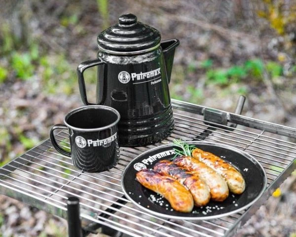 Percolator negru Petromax, cana si farfurie cu carnati asezate pe un grilaj